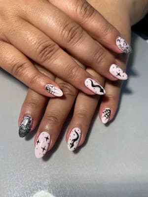 Pale pink almond nails with black spiderwebs, ghosts, crosses, and silver glitter accents.